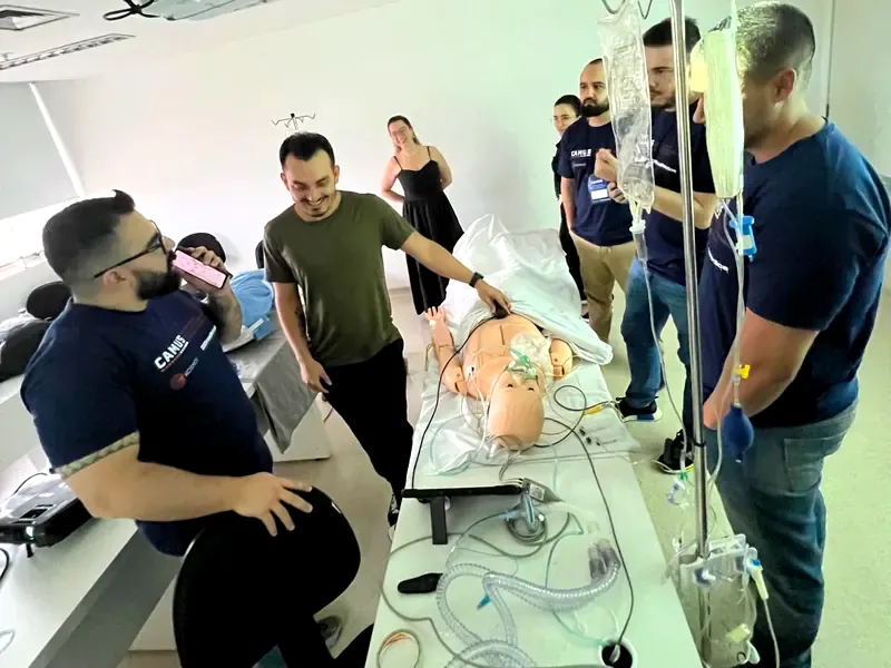 Laboratório de simulação: instrutores e alunos em volta de um manequim, com monitores e equipamentos