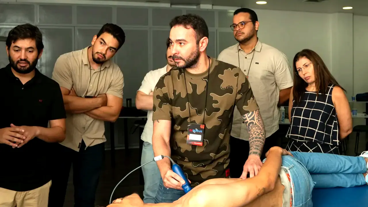 Treinamento presencial do IMPOCUS: instrutor escaneia um voluntário deitado na maca enquanto a turma acompanha